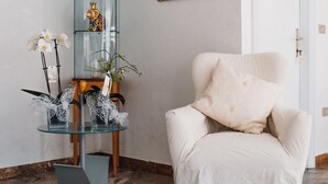 A room with a glass display cabinet, a chair with a cushion, a patterned rug, and a framed portrait on the wall. - Hotel Morri's (Rimini)