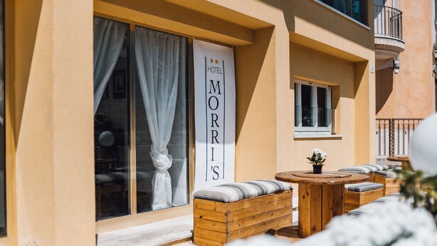 A hotel named "MORRIS'S" with a wooden bench seating area and a small table. - Hotel Morri's (Rimini)