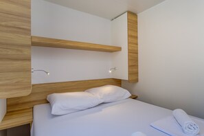A modern hotel room with a wooden headboard, a neatly made bed with white linens, and a towel on the side.