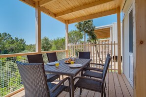 A covered outdoor dining area with wicker chairs and a table set for two, overlooking a fenced garden.