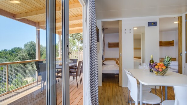 Ein modernes Zimmer mit Holzboden und einer Terrasse, einem Bett mit weißem Kopfteil, einem Esstisch mit Stühlen und einer Obstschale.