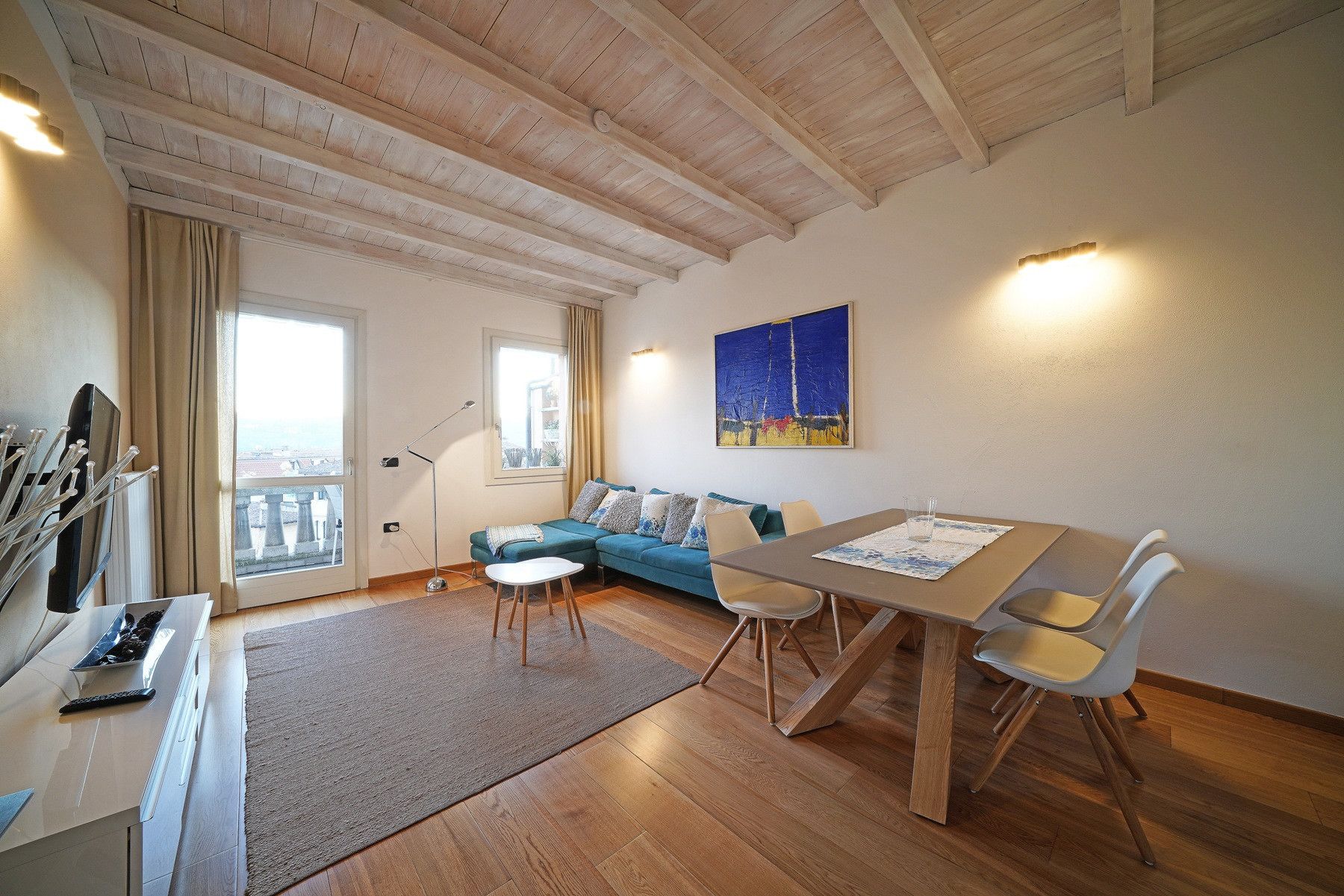 Ein gemütliches Wohnzimmer mit Holzbalkendecke, einer Couch, einem Esstisch mit Stühlen und einem Bild an der Wand.