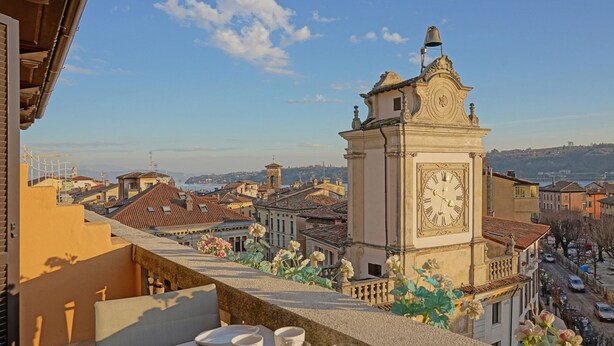 Un balcone con tavolo apparecchiato per mangiare, vista su un panorama urbano con edifici storici e una torre dell'orologio ben visibile.