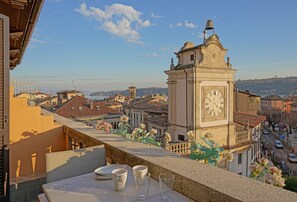 A balcony with a table set for dining, overlooking a cityscape with historic buildings and a prominent clock tower.