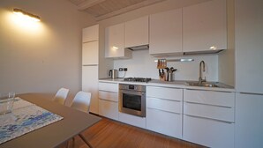 Una cucina moderna con mobili bianchi, forno integrato, piano cottura e lavello in acciaio inossidabile.
