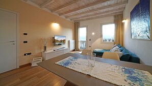 Un soggiorno moderno con soffitto in legno, una TV a parete, un divano, un tavolo da pranzo con tovaglietta e un quadro appeso al muro.