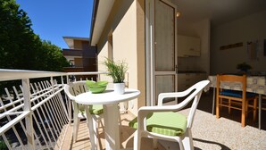A balcony with a table and two chairs, a potted plant, and a view of the building's interior. - Villa Gaby (Lignano Sabbiadoro)