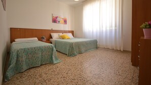 A room with two beds, a wooden headboard, a painting on the wall, and a window with curtains. - Villa Gaby (Lignano Sabbiadoro)