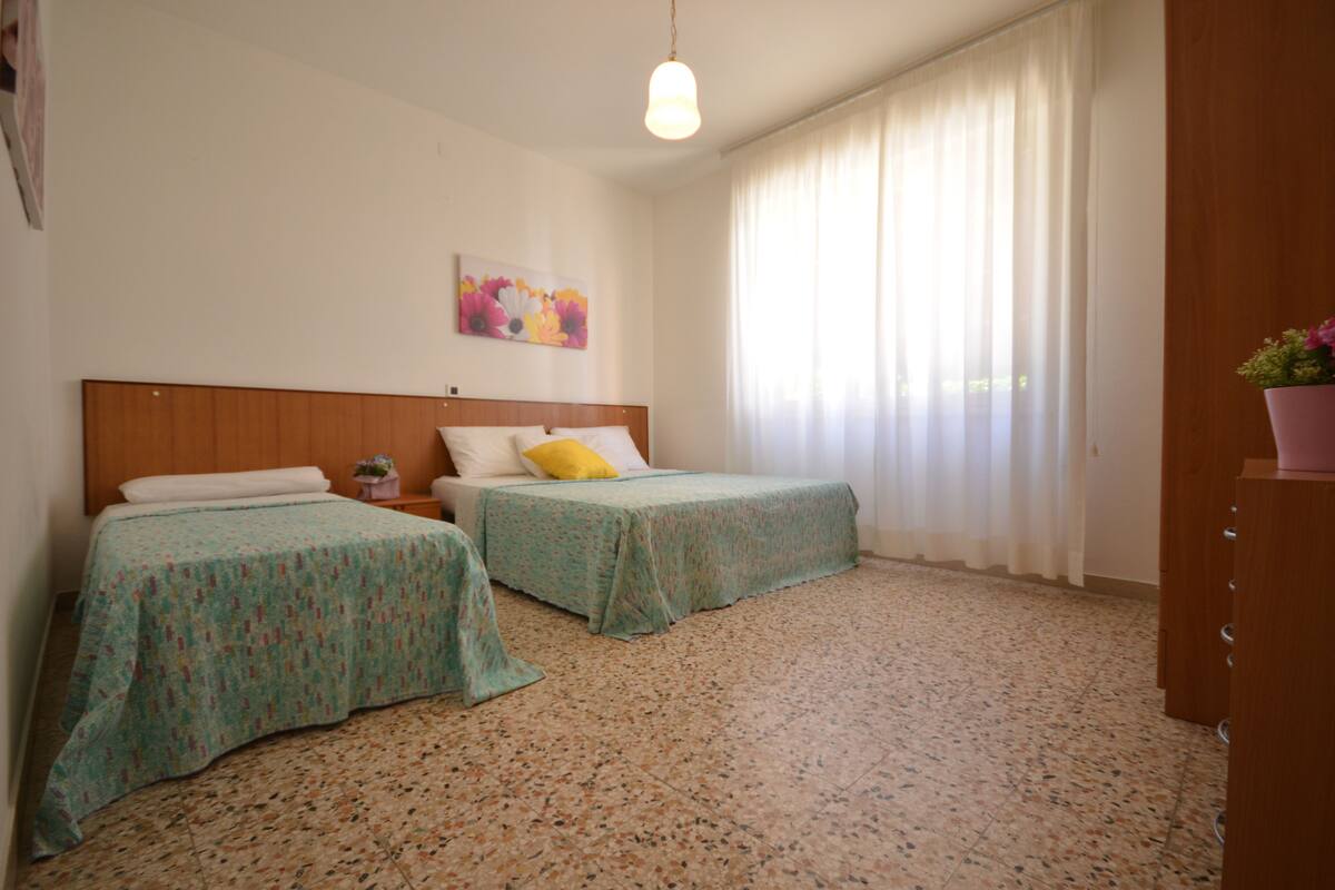 A room with two beds, a wooden headboard, a painting on the wall, and a window with curtains.
