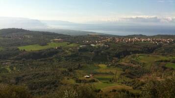 Vista panorámica de un paisaje montañoso con un pueblo a lo lejos, rodeado de vegetación y campos.