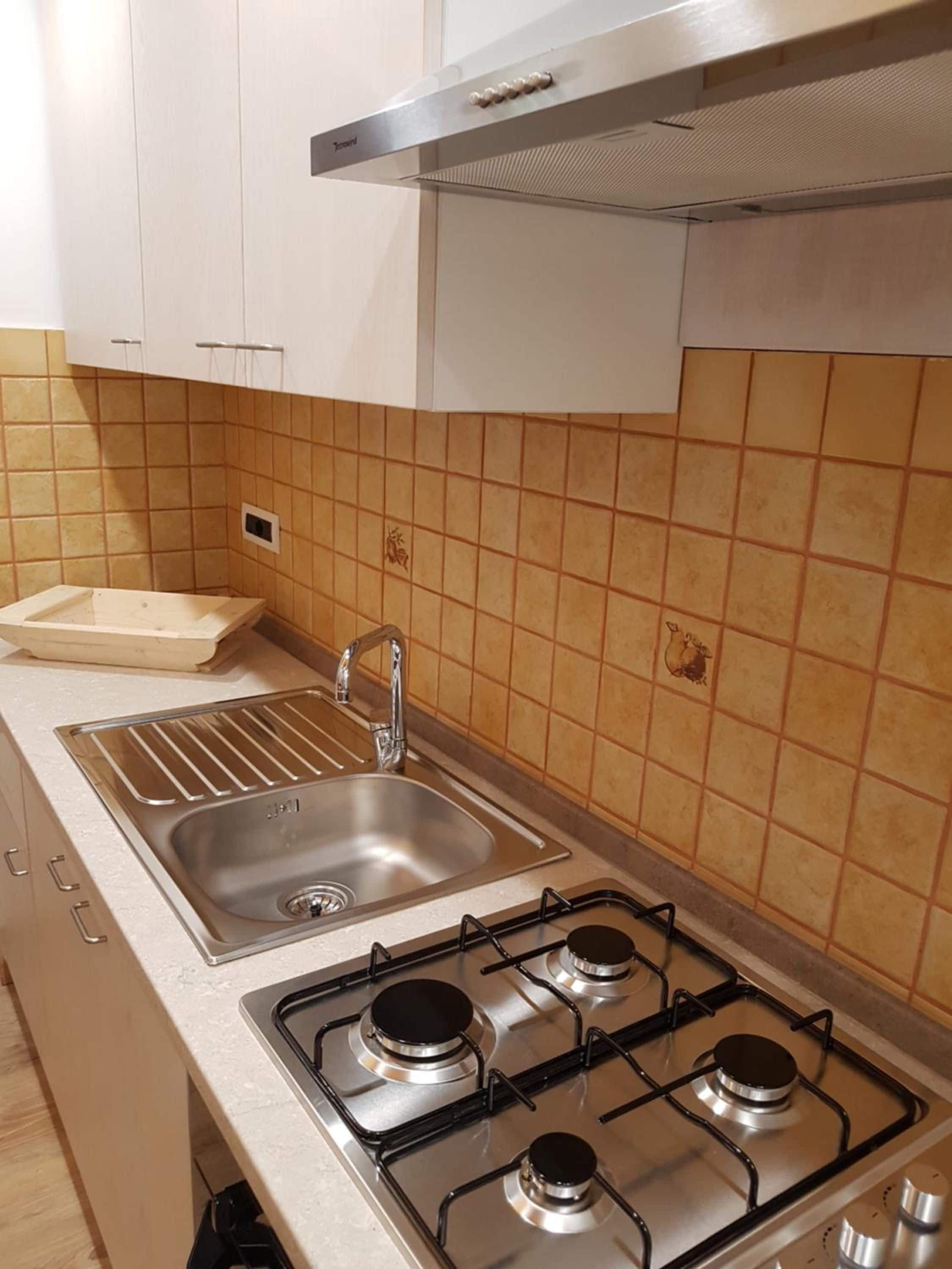 Een keuken met een dubbele spoelbak, een fornuis met vier gaspitten en witte keukenkastjes.