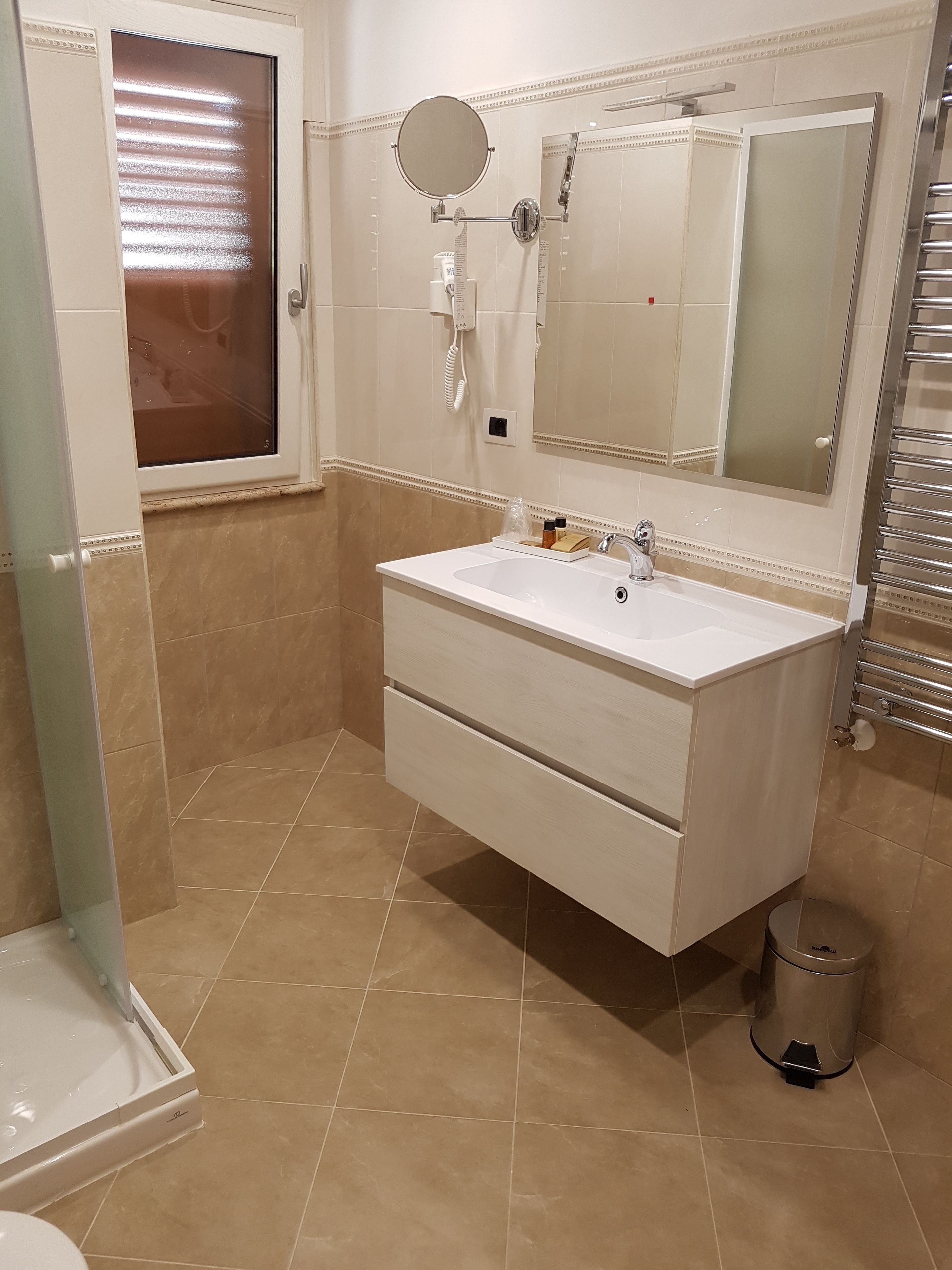 Une salle de bain avec un meuble-lavabo blanc, un grand miroir, des toilettes et une poubelle.