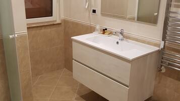 Une salle de bain avec un meuble-lavabo blanc, un grand miroir, des toilettes et une poubelle.