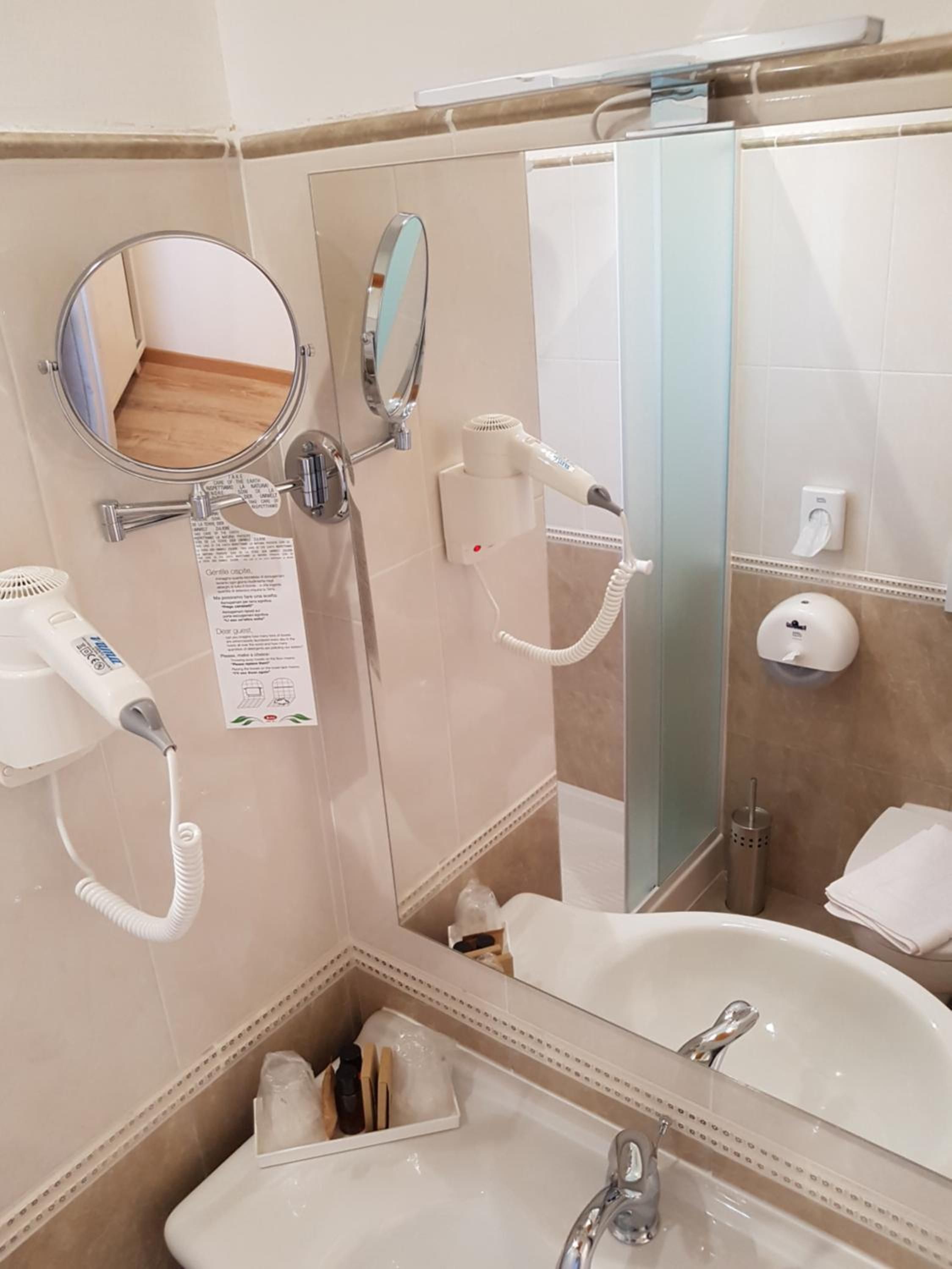 A bathroom with a sink, mirror, hairdryer, and a hand dryer.