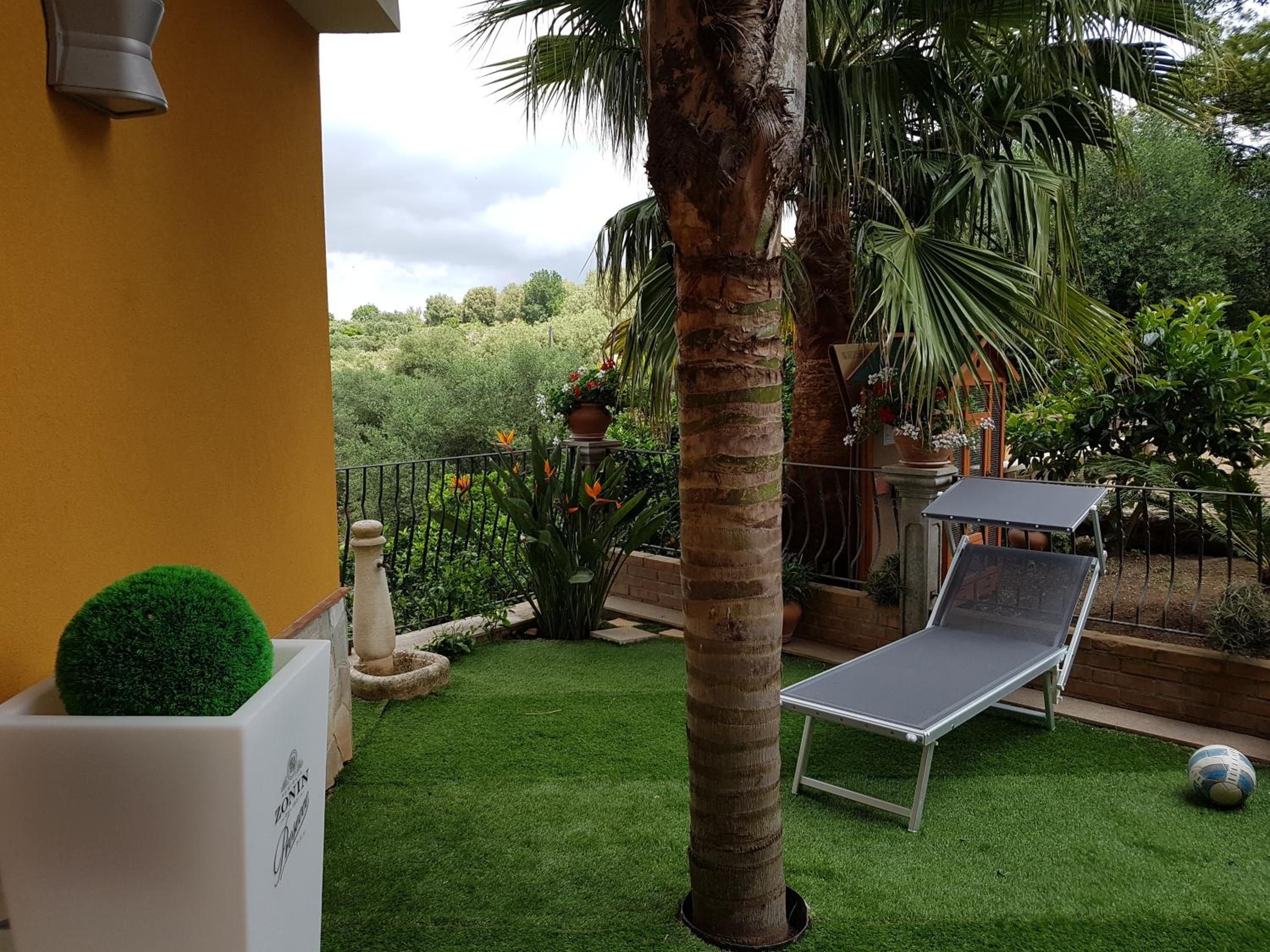 Une terrasse avec un revêtement de gazon synthétique, un fauteuil de relaxation, une table et un petit pot de fleurs rond.