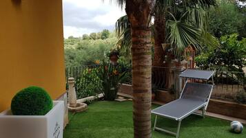 Une terrasse avec un revêtement de gazon synthétique, un fauteuil de relaxation, une table et un petit pot de fleurs rond.