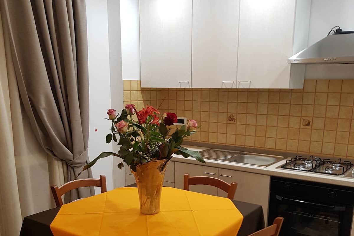 A compact kitchen with white cabinets, a gas stove, and a dining table with a yellow tablecloth.