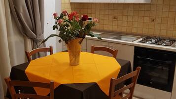Une cuisine de taille réduite, avec des meubles blancs, une cuisinière à gaz et une table à manger recouverte d’une nappe jaune.