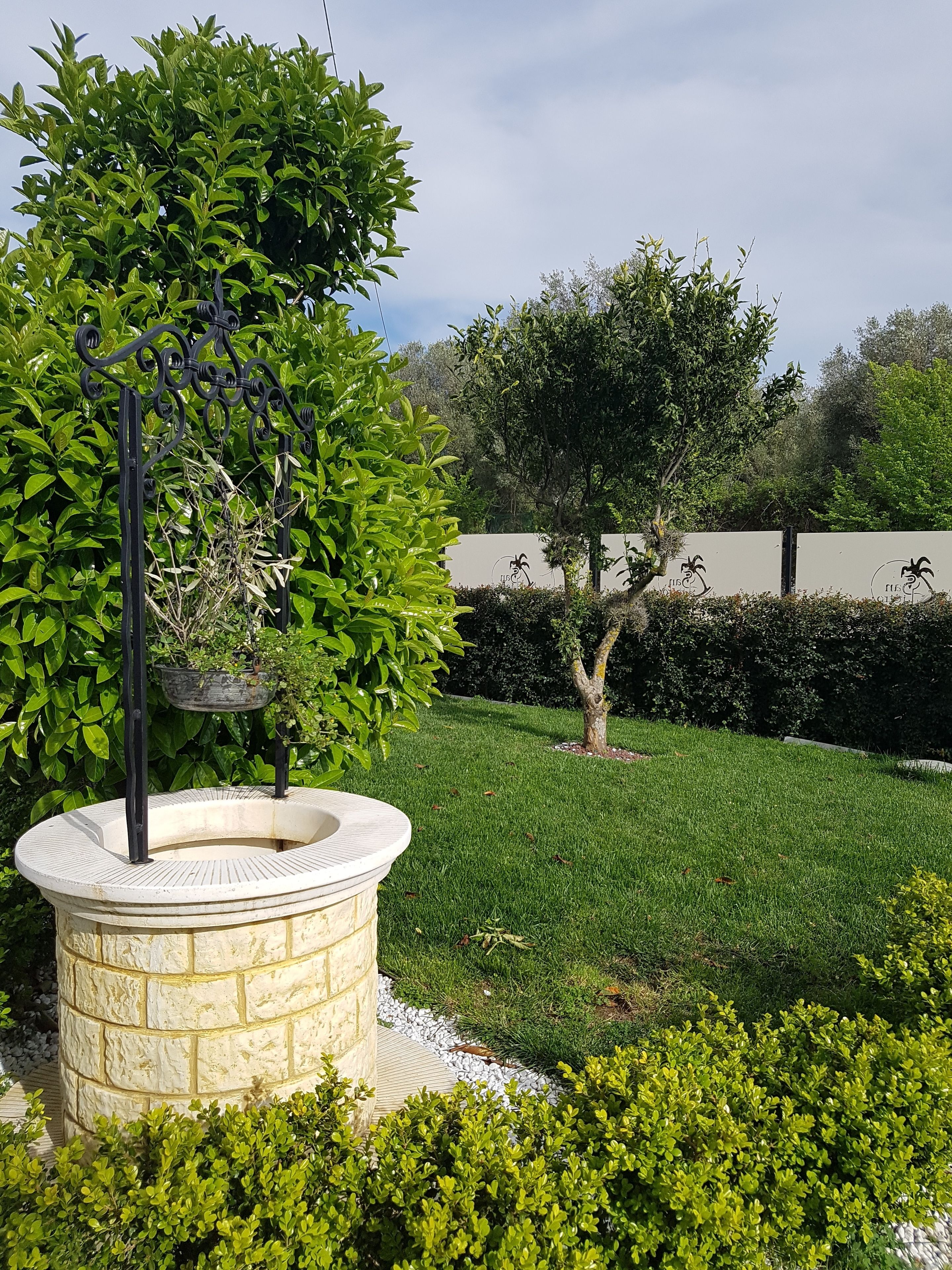 A well-maintained garden with a stone fountain, neatly trimmed hedges, and a variety of trees.
