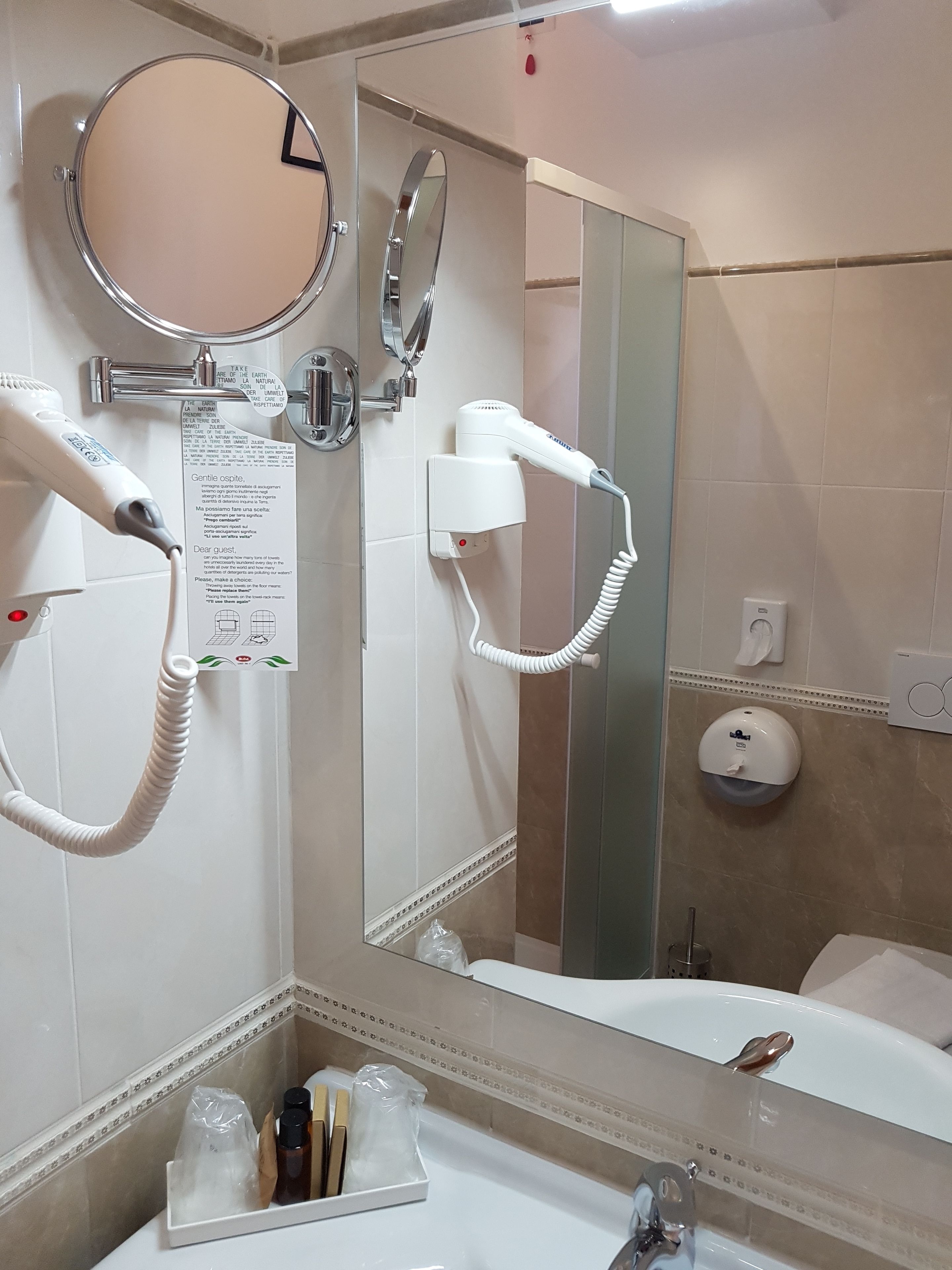 A bathroom with a hairdryer, a mirror, a hand dryer, and a soap dispenser.