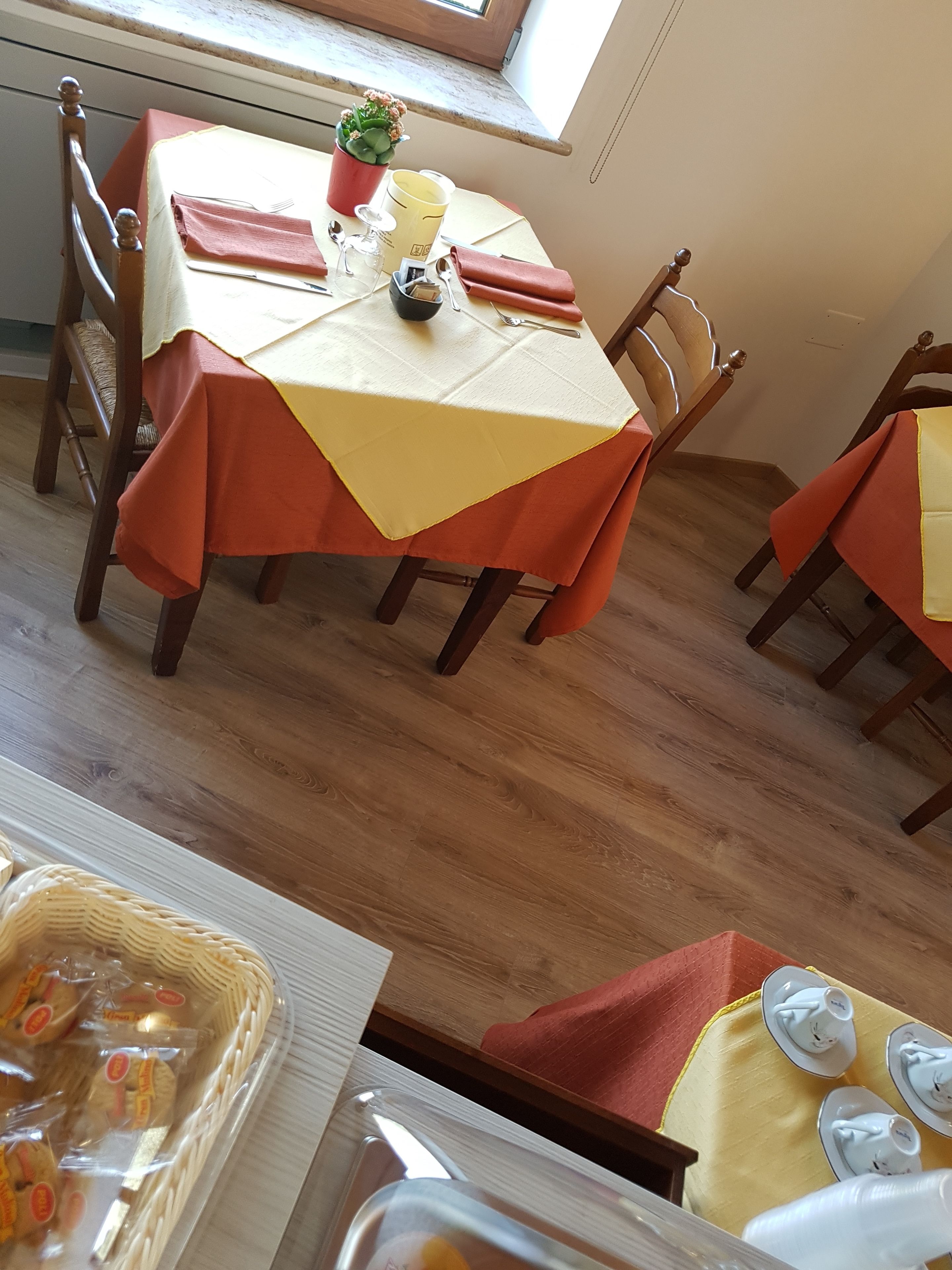 A dining area with a table set for two, featuring a yellow tablecloth, red napkins, and a potted plant.