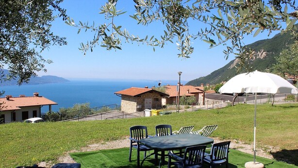 A terrace with a table and chairs, overlooking a coastal view with houses and a white dome structure.