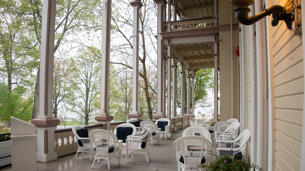 A covered porch with white wicker chairs and a potted plant. - Athenaeum Hotel (Mayville)