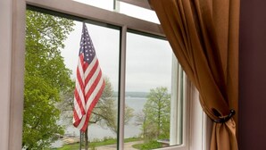 A window with an American flag and a view of a lake and trees. - Athenaeum Hotel (Mayville)