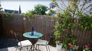Eine Terrasse mit einem runden Tisch und zwei Stühlen, umgeben von einem Holzzaun und Topfpflanzen.