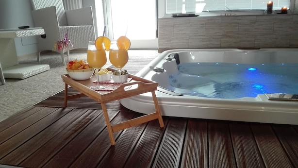 Une table en bois avec un saladier de fruits, un verre et une bougie. On aperçoit un jacuzzi à l’arrière-plan.