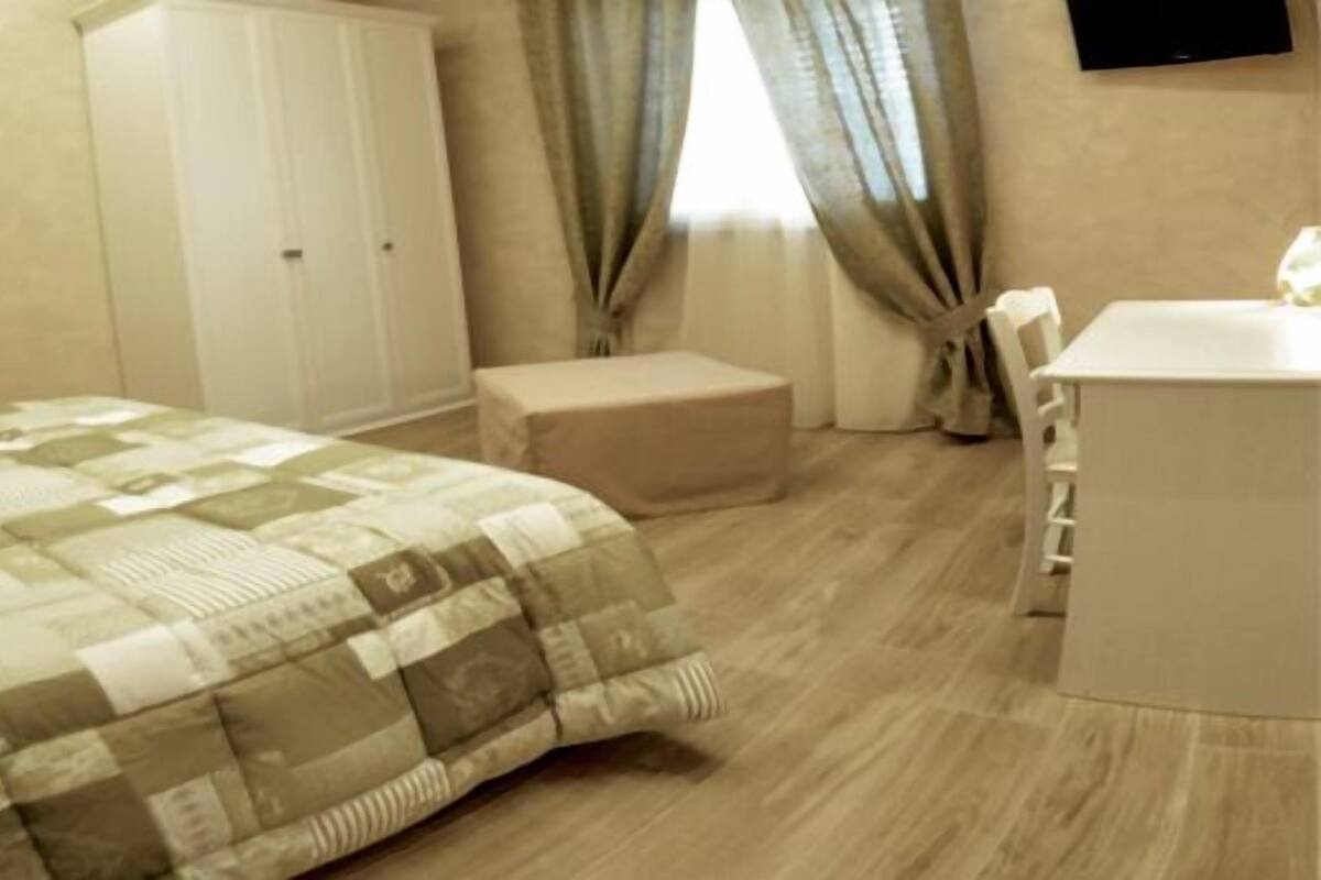 A hotel room with a bed, a small desk, a wardrobe, and a window with curtains.