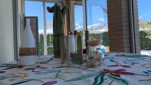 Un balcon avec une table recouverte d’une nappe à motifs floraux, un vase blanc, un chandelier et une bougie en verre.