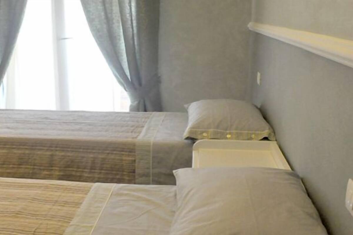 A room with two beds, a small table, a TV mounted on the wall, and a window with curtains.