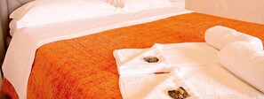 A bed with white sheets and an orange quilt, a white bathrobe, and a white towel on the bed. - La Villetta sul Mavone (Colledara)