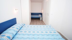 Ein schmales Zimmer mit einem Bett links und einem kleineren Bett im Hintergrund.