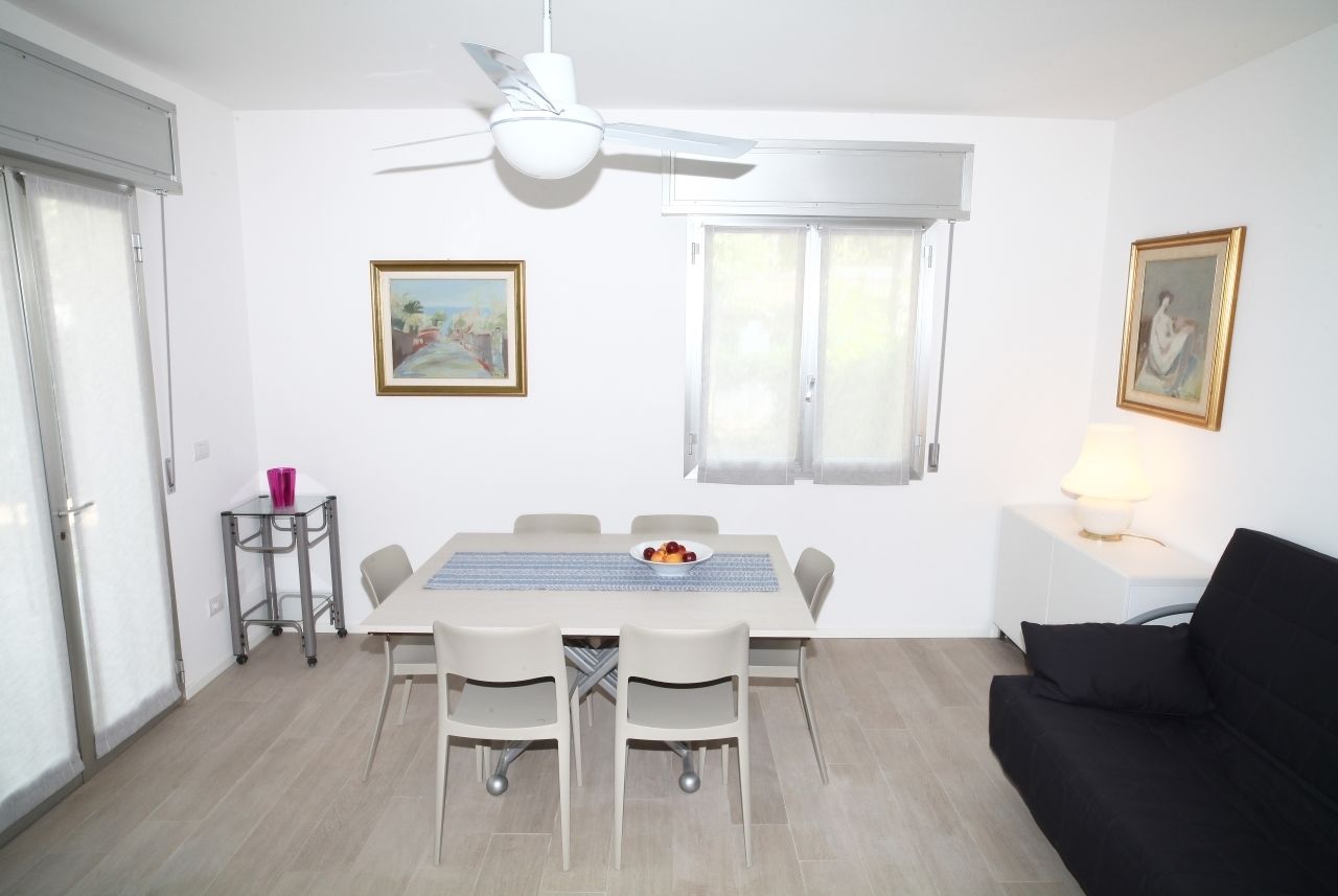 Een eetruimte met een tafel, stoelen, plafondventilator en twee ramen.