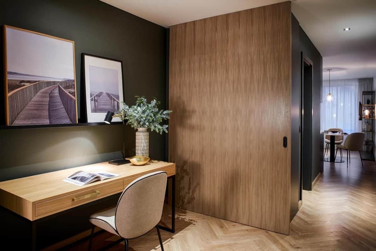 A modern office space with a wooden desk, a chair, a vase with plants, and framed pictures on the wall.