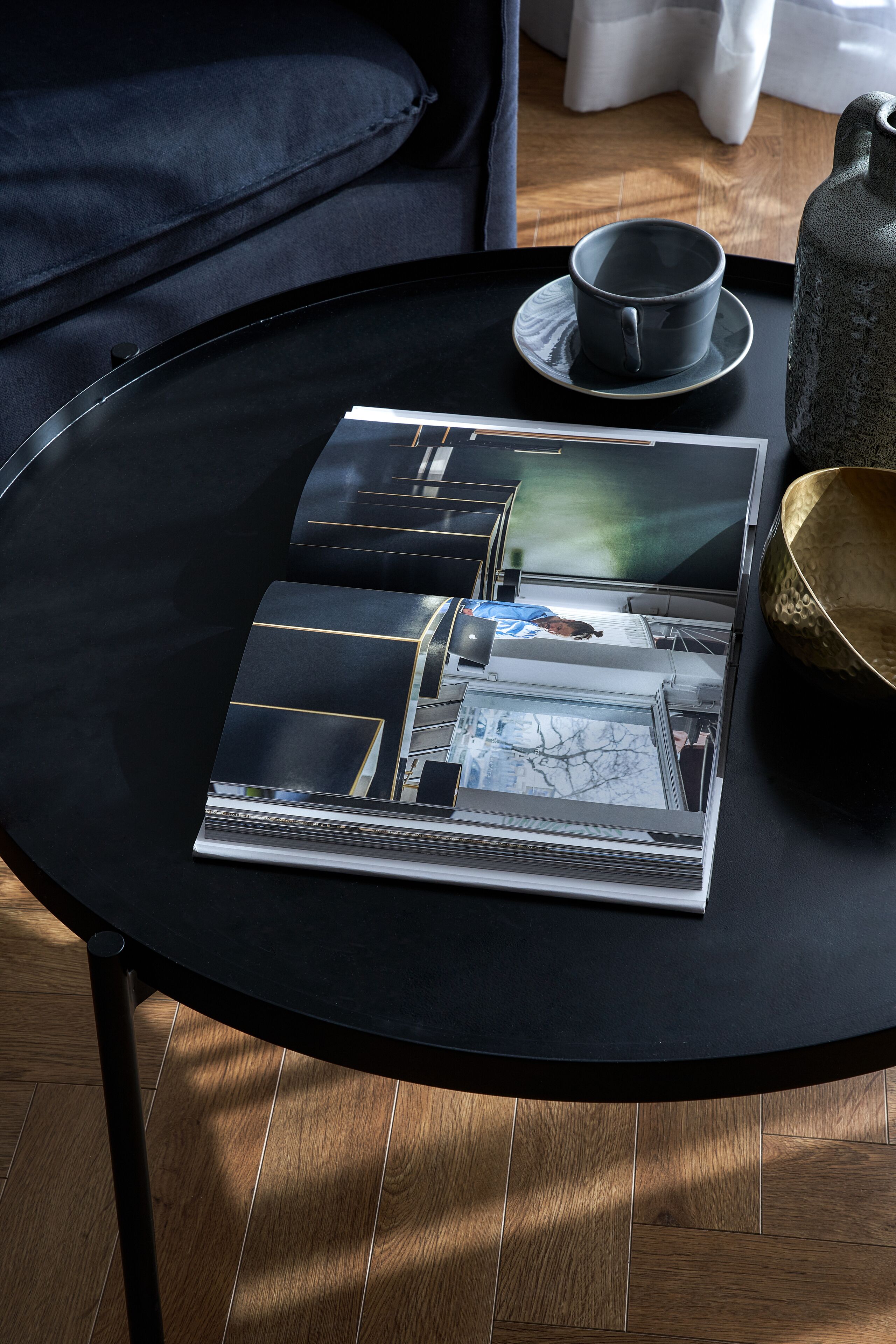 A black table with a magazine, a cup, and a vase.