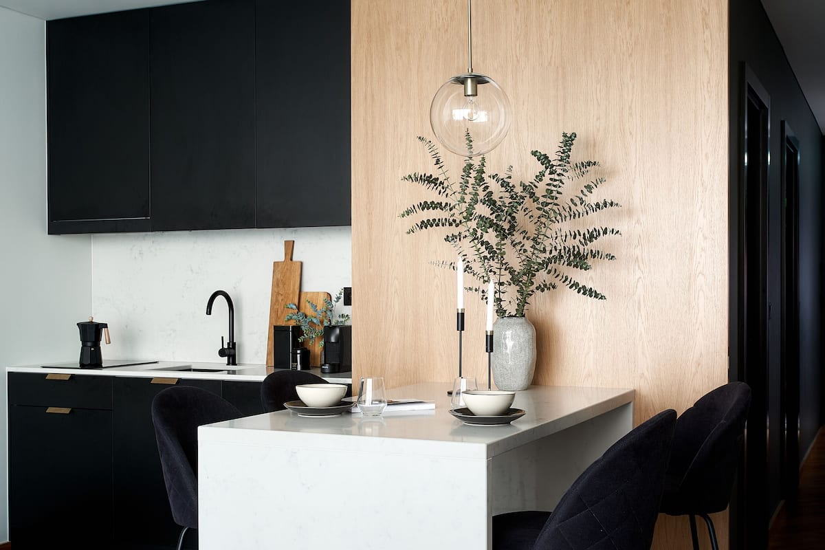 A modern kitchen with a central island, black cabinets, and a wooden accent wall.