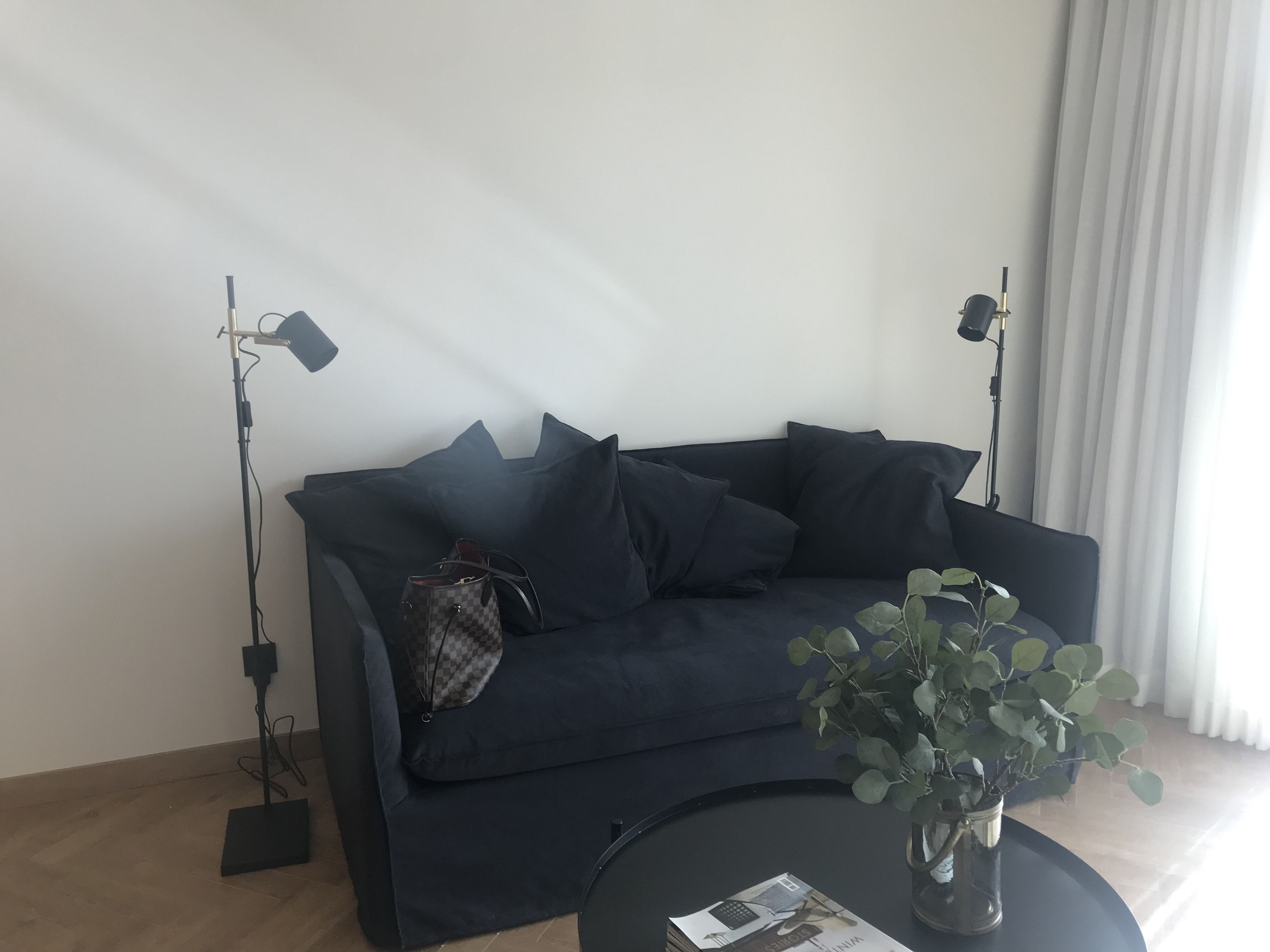 A dark blue sofa with multiple cushions, a small checkered bag, a potted plant, and two floor lamps.