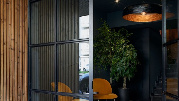 Un intérieur moderne avec un sol à carreaux, un mur lambrissé en bois, une plante en pot et un coin salon avec un fauteuil.
