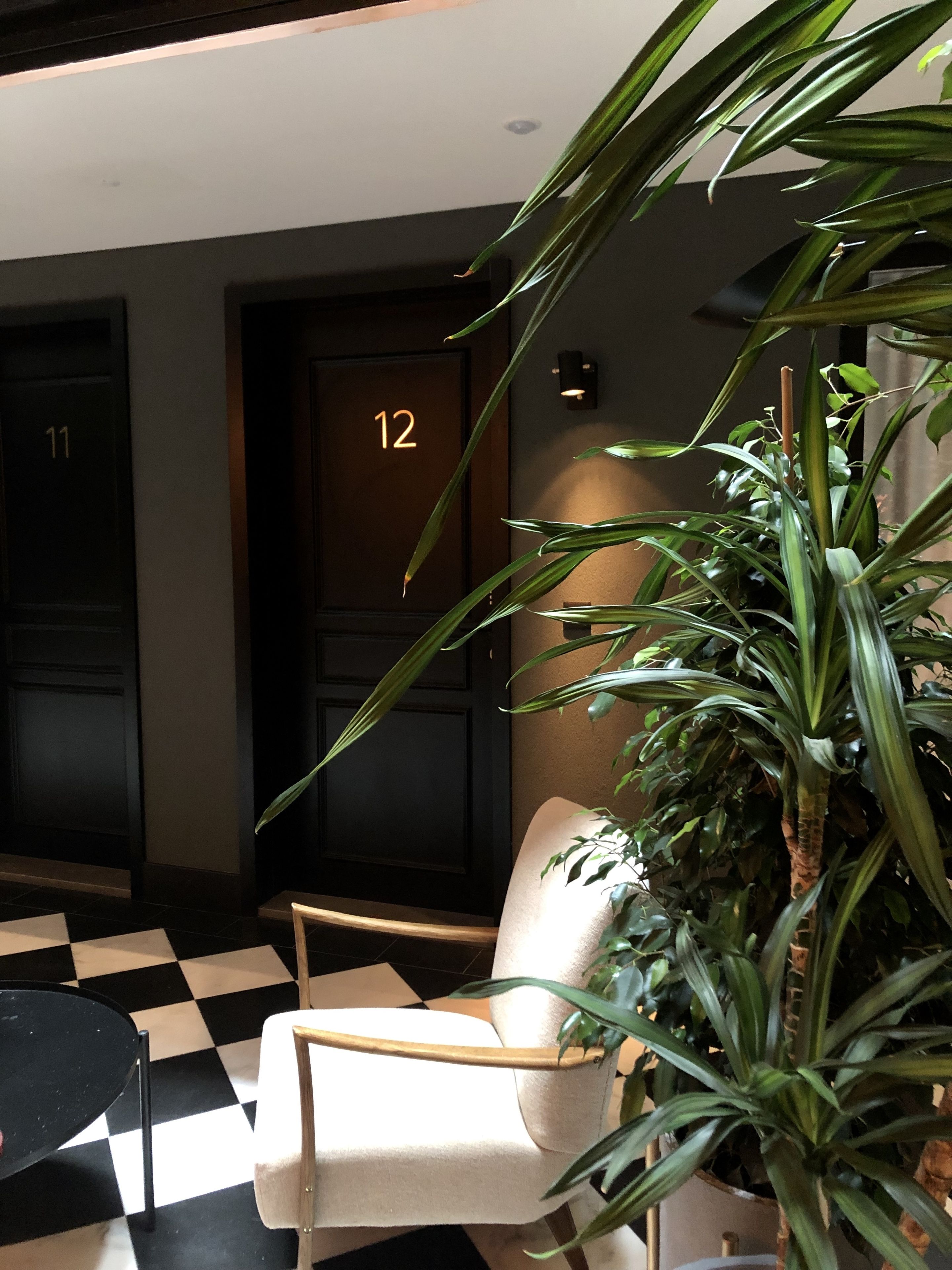 A lobby with a checkered floor, a white armchair, a potted plant, and doors numbered 11 and 12.