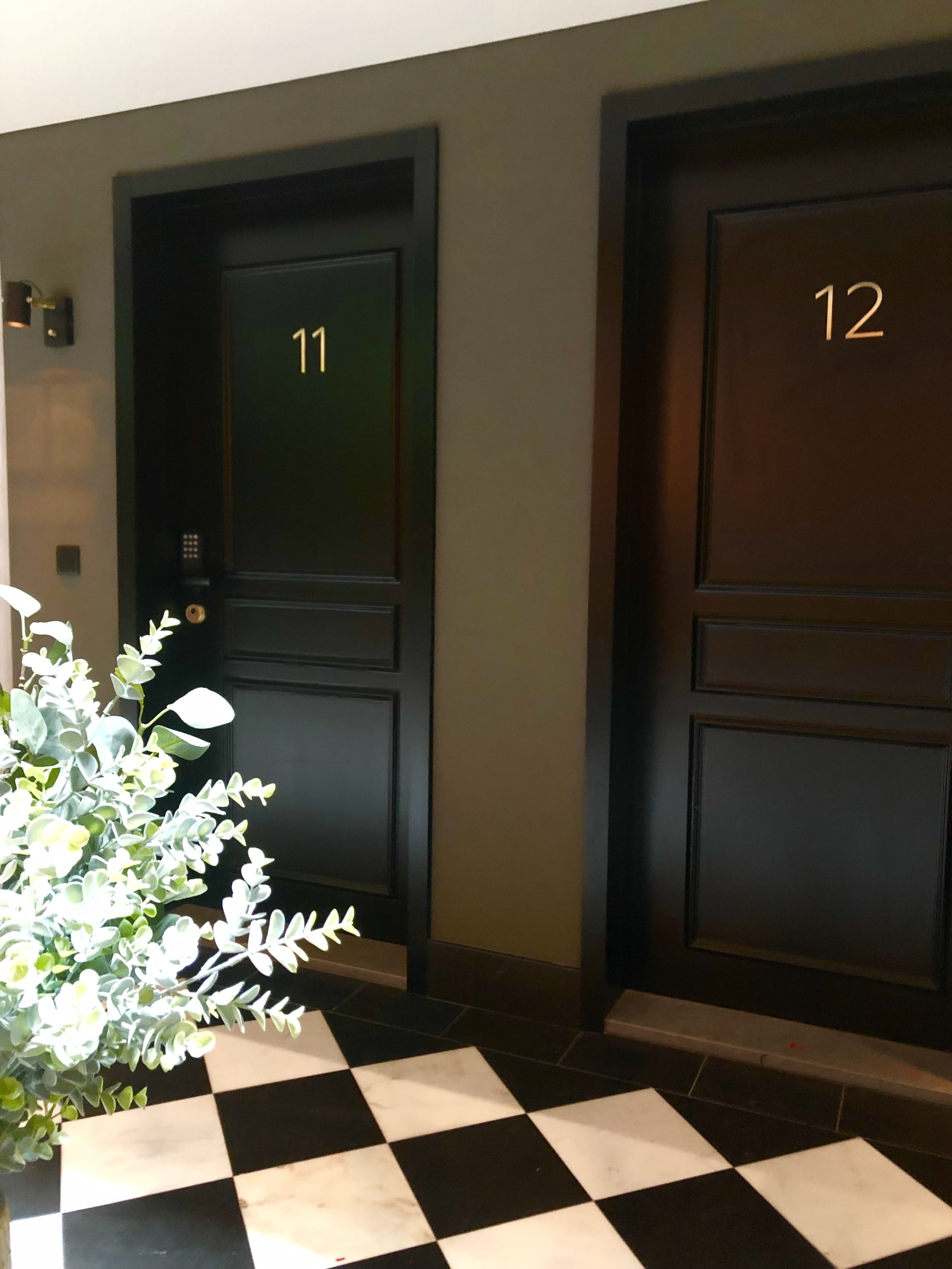 Two dark wooden doors with numbers 11 and 12, a checkered floor, and a potted plant with white and green leaves.