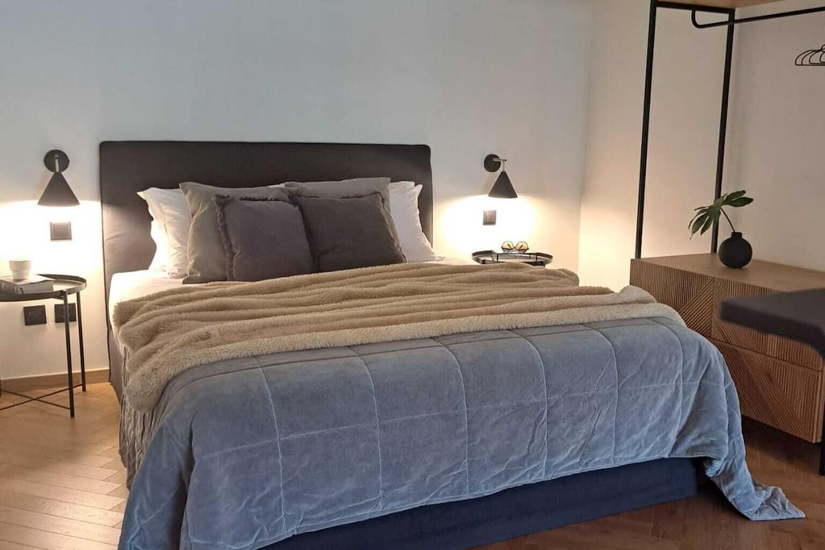 A modern bedroom with a large bed, two bedside tables, a hanging plant, and a wooden floor.