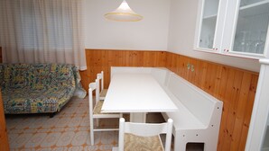 A small, cozy room with a white table and benches, a patterned sofa, and a window with a white frame. - Villa Isolina (Lignano Sabbiadoro)