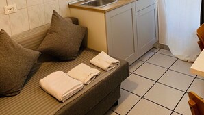 A compact kitchenette with a sink, cabinets, and a countertop. There is a sofa with cushions and a rolled-up towel. - Bed2Go (Turin)