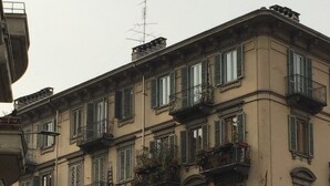A multi-story building with balconies, parked cars, and a pedestrian. - Bed2Go (Turin)