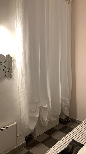 A room with a checkered floor, a bed with a striped bedspread, and a white curtain with a bow tied at the bottom. - Bed2Go (Turin)