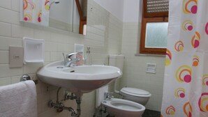 A bathroom with a sink, toilet, and bidet, tiled walls, and a shower curtain with a colorful pattern.