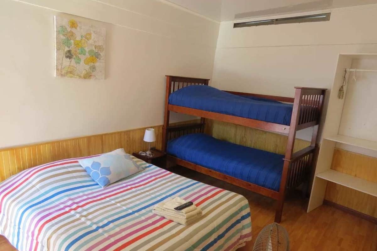 Ein Zimmer mit einem Etagenbett, einer gestreiften Bettdecke, einem kleinen Tisch mit einer Lampe und einem Stuhl.